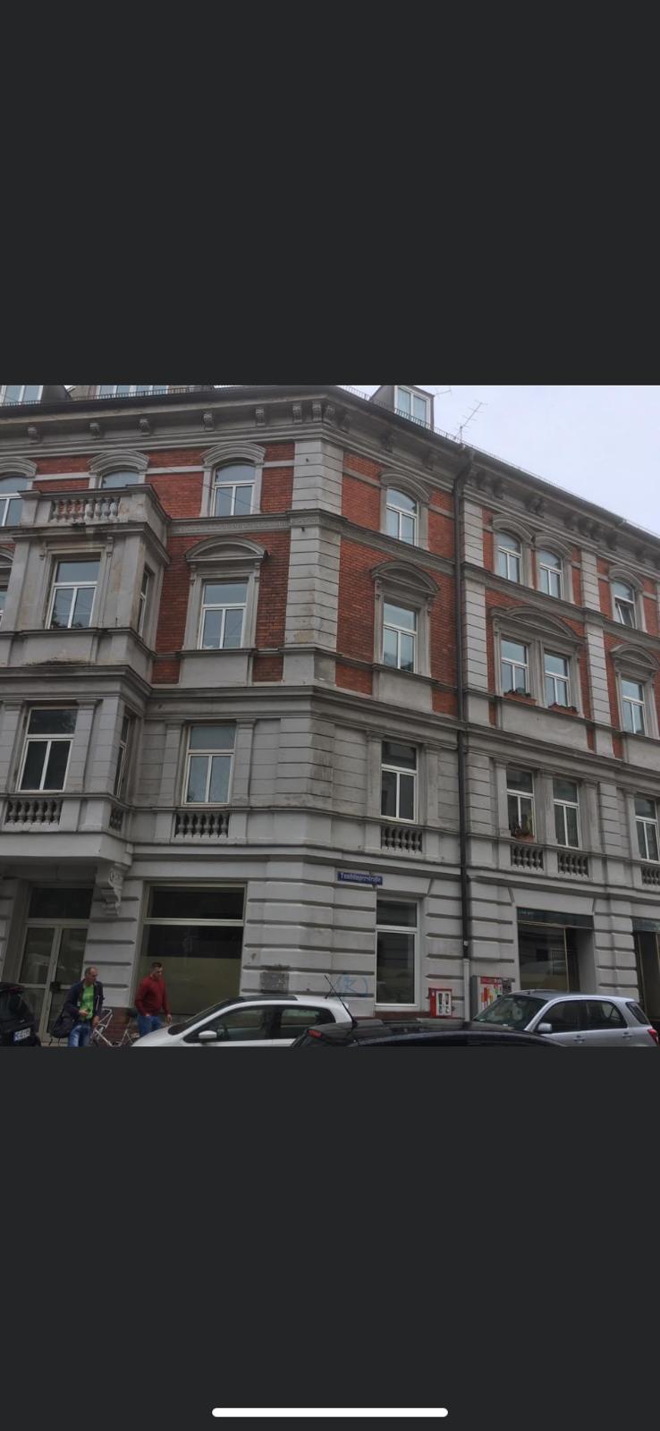 Historische Eckfassade mit grauen Putzflächen und rotem Ziegel vor der Sanierung